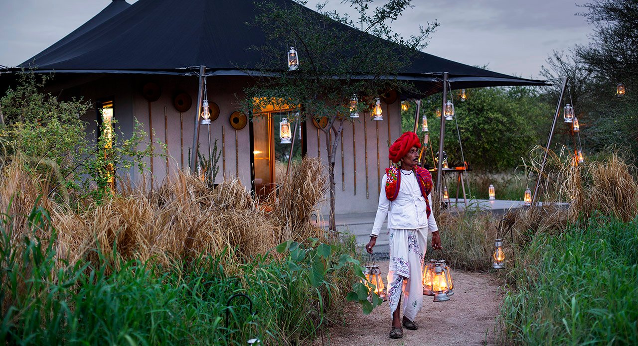Rabari host carrying lanterns outside a luxury safari tent near Jawai